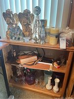 Full view of wooden bookshelf with all shelf contents including statues, candles, bags, vases and figurines.