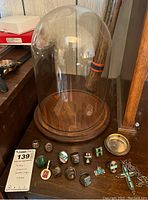 Multiple sterling silver rings with various stone inlays arrayed on wood surface alongside glass dome, pocket watch case, cross necklace