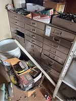 Photo showing the full view of a large vintage multi-drawer metal cabinet with several drawers and boxes of hardware on top, including nails and screws.