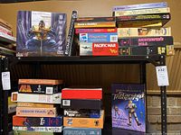 Wide view of 26 assorted vintage tabletop role-playing and tactical war games in their original boxes stacked on shelves.