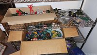Two cardboard boxes on metal shelving containing various vintage toys including army men in different colors and other miniature figures.