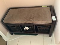 Full view of the bamboo hall bench with cushioned top and three bamboo baskets underneath, placed in a corner on tiled floor.