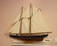 Front view of the Bluenose model ship showing sails fully raised, black hull with white trim, and wooden display stand.