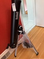 Telescope mounted on tripod with Bushnell protective tube hung on the tripod.