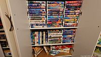 Shelf packed with Disney VHS tapes - various titles stacked horizontally and vertically in a white shelving unit