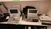 Photo showing Equinox and multifunction portable DVD players with screens, remotes, and accessories on a shelf.
