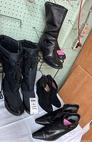 All four pairs of boots displayed on a table against a wall, showing black winter snow boots, tall leather boots, black suede wedge ankle boots, and leather pointed toe ankle boots.