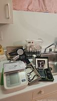 Full lot image showing blood pressure monitor, stethoscope, several boxed items, bags with curlers, and various personal care devices arranged on a kitchen counter.