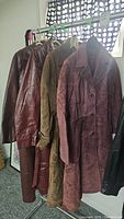 Three vintage ladies coats hanging on rack, showing two brown leather and one maroon suede coat.