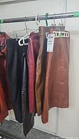 Row of five vintage leather and suede skirts hanging on rack. Colors include black, burgundy, tan, and brown.