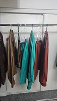 Leather jackets and pants hanging on a rack showing brown, teal, and reddish leather garments.