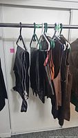 Black and brown leather pants, chaps, and vests on hangers, displayed on clothing rod