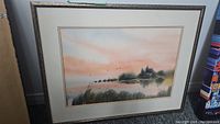 Full view of matted and framed watercolor painting leaning against wall