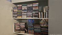 Shelves filled with numerous cassette tapes and CDs stacked and organized horizontally and vertically.