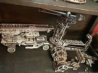 Wooden mechanical 3D fire ladder truck model with extended ladder and visible gear mechanisms on a shelf.