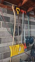 Snow shovels, ice breakers, car shovel, and fishing net hanging on a concrete block wall inside a wooden shed.