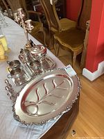 Photo showing the silver plate serving set arranged on a table, including the meat or fish platter with divider, candelabra, and tea service pieces on trays.