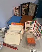 Overview of four stamp albums, stacks of country-labeled envelopes, plastic bags of stamps and red tweezers