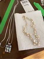 Two necklaces placed next to a lot tag labeled 'Sterling'. One necklace has a rectangular multi-colored mother of pearl pendant on a silver chain, the other is a double-strand freshwater pearl necklace.