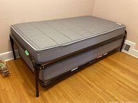 Full view of the twin size trundle bed with black metal frame and top mattress cushioned in gray fabric.