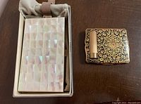 Two vintage makeup cases placed side by side on a wooden surface inside a cloth-lined box for the larger case, smaller case on the right.