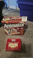 Photo showing original boxes of Ohio Art The Animator and Nintendo Mario Bros Game & Watch Multi Screen on carpet floor.