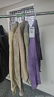 Five vintage suede coats in various muted colors hanging on a metal rack against a white wall with polka dot curtain in background