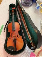 Violin inside a black hard case with green velvet interior alongside two bows and rosin, lying open on a surface.