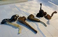 Overview photo of six assorted smoking pipes with wood and whimsical designs, showing variation in size and style.