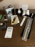 Eight watches displayed on table, including one in Voit tin, one in Skagen box, others on stands or flat with varying band materials and colors.