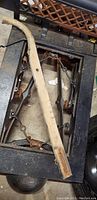 Close-up of heavy black metal frame with wooden handle resting across it, showing incomplete missing wooden scale bed and parts.