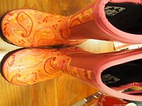 Top view of orange girls' rain boots with floral pattern and pink elastic side panel, showing toe and upper surface details.
