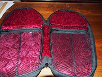 Open view of coffin-shaped drumstick case showing red quilted interior and mesh pockets.