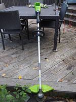 Full view of the GreenWorks battery operated string trimmer laid out on wooden deck with adjustable handle and guard visible.
