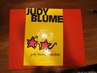 Yellow box with 'Judy Blume Essentials' text and two red star illustrations on top of an orange box.