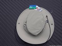 Top-down photo of beige Tilley XL sun hat with original tag and strap detached on one side, showing overall shape and material texture.