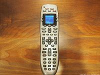 Front view of the Logitech Harmony 650 remote showing the LCD screen and various buttons on a wooden surface.