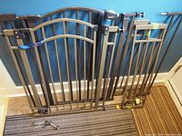 Two black expandable metal safety gates leaning against a blue wall, showing vertical bars and latch mechanisms.