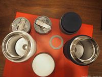 Top view of interior and lids of two thermos containers showing stainless steel inner walls, rubber sealing rings, screw caps, and wrapped sporks