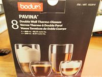 Photo of Bodum Pavina product packaging showing box with images of 8 double wall thermo-glasses, 4 large and 4 small sizes, with product details in multiple languages