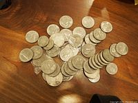 Top view of coins spread on wooden surface showing mixed Canadian and US coins, mostly silver dollars and 50 cent pieces.