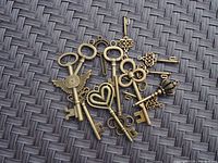 Nine decorative brass-tone metal steampunk style keys arranged on woven surface, showcasing various ornate and themed bows including wings, hearts, and skulls.