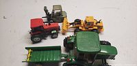 Photo showing five toy models including a green John Deere die cast tractor, yellow Caterpillar bulldozer, olive Clark forklift, red tractor, and a green trailer with a yellow rake attachment.