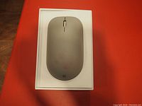 Top view of the gray Microsoft Surface Mouse showing the button and scroll wheel layout on a white tray background.