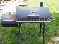 Side view of used offset wood smoker BBQ grill with black metal body showing surface rust and attached smaller offset firebox on left side, main lid closed.