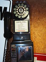 Front view of black Crosley rotary telephone replica with 1957 dial, coin slot, and local call rate signage.