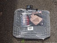 Image of the packaged set of two gray WeatherTech rear floor mats, model W20GR, on an outdoor ground surface.