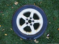 Single silver one-piece 5-spoke Volvo alloy rim with mounted Michelin X-Ice tire lying on grass showing road rash and edge wear.