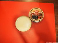 Top-down photo of an opened round tin showing white mink oil wax inside and the lid next to it with Kiwi branding and product details.