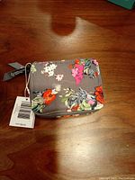 Closed floral Vera Bradley travel pill case with tags attached, sitting on wooden surface.